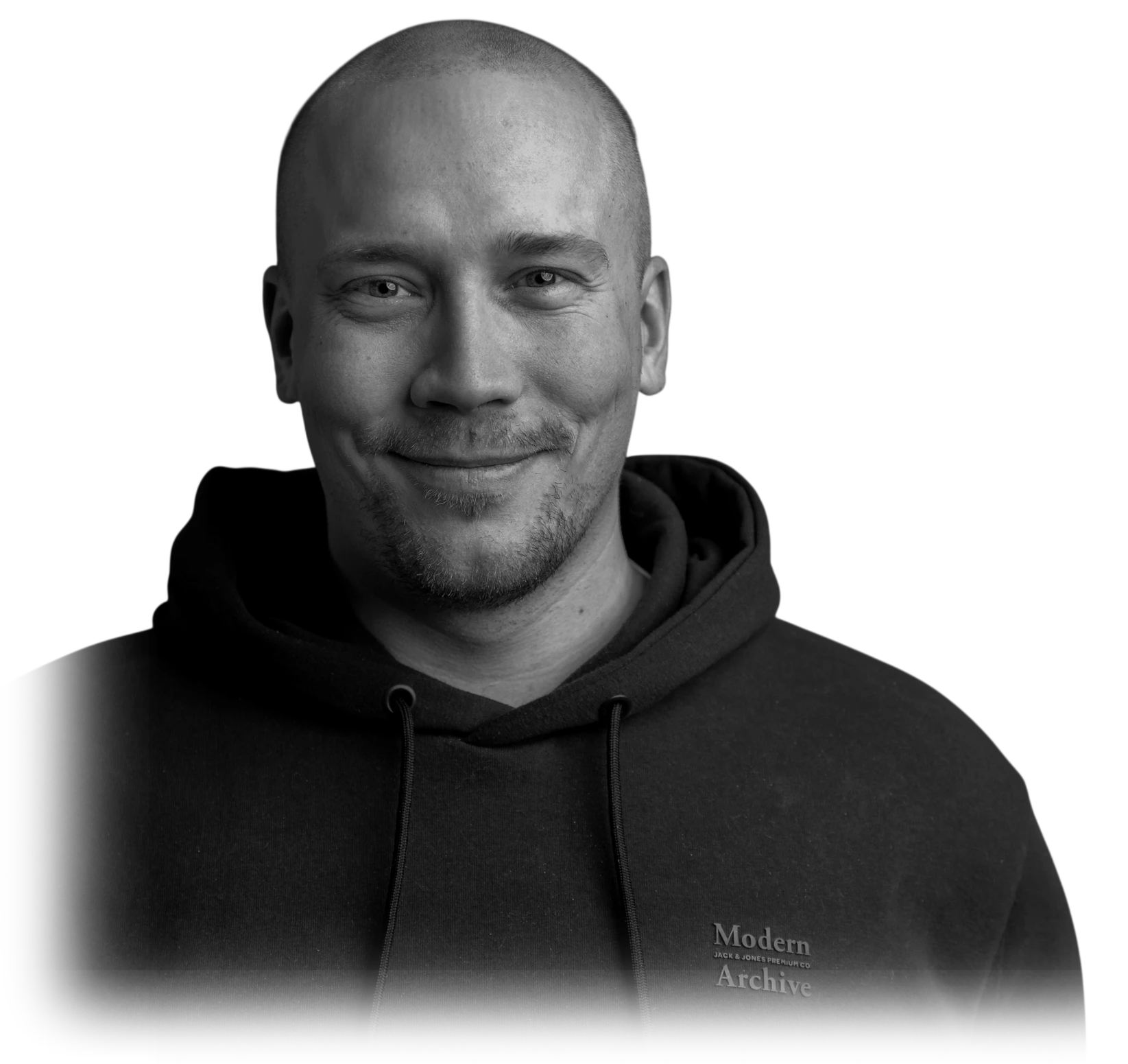 Mustavalkoinen muotokuva: Mikko hymyilee tummassa hupparissa.